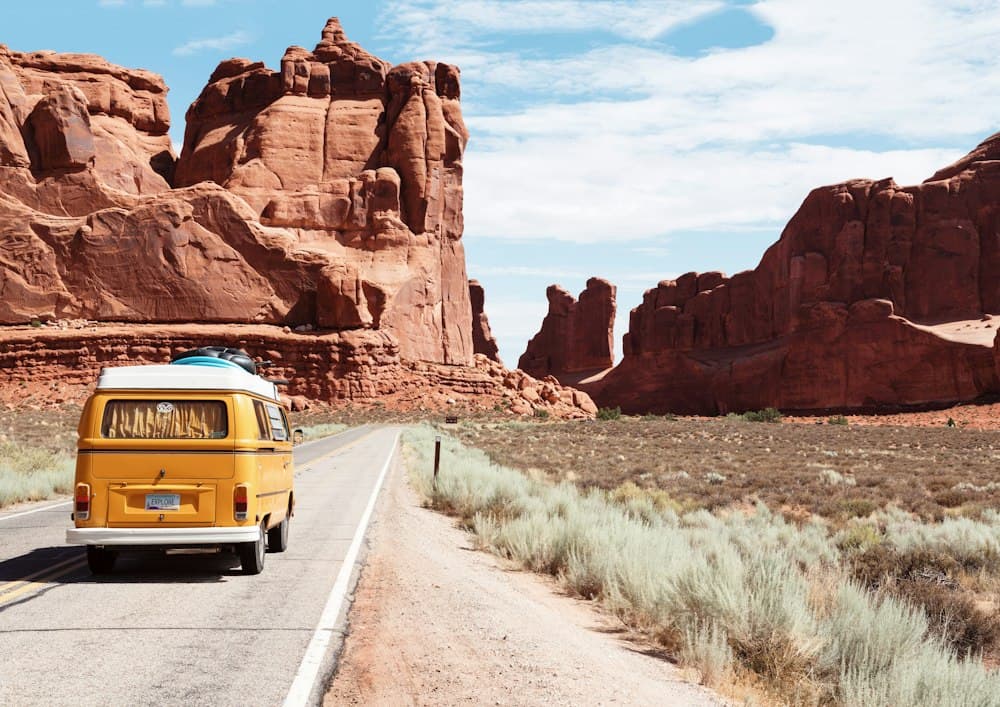 Yellow camper van driving along a desert road past red rock cliffs