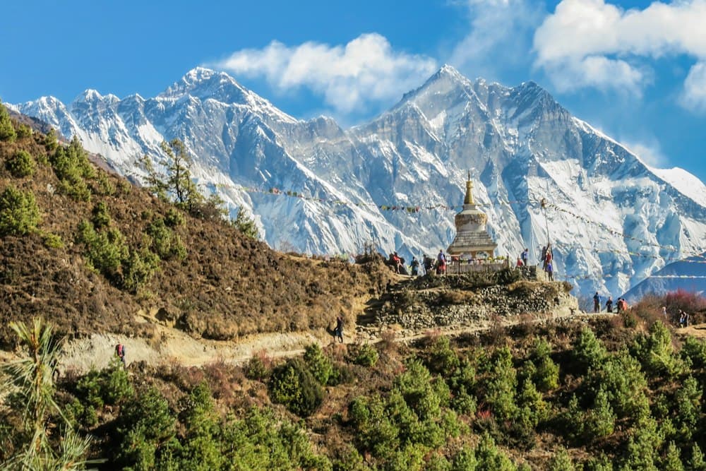Snow-covered Himalayan peaks above a hillside trail and stupa