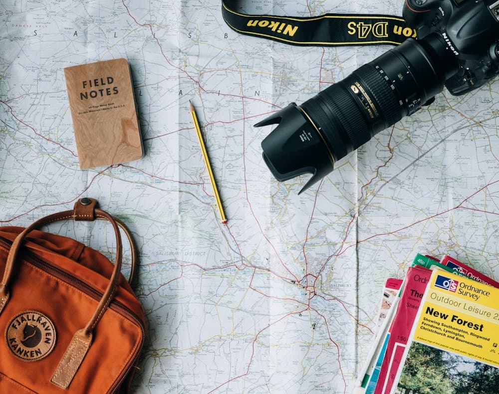 Map, camera, notebook and backpack laid out for a trip