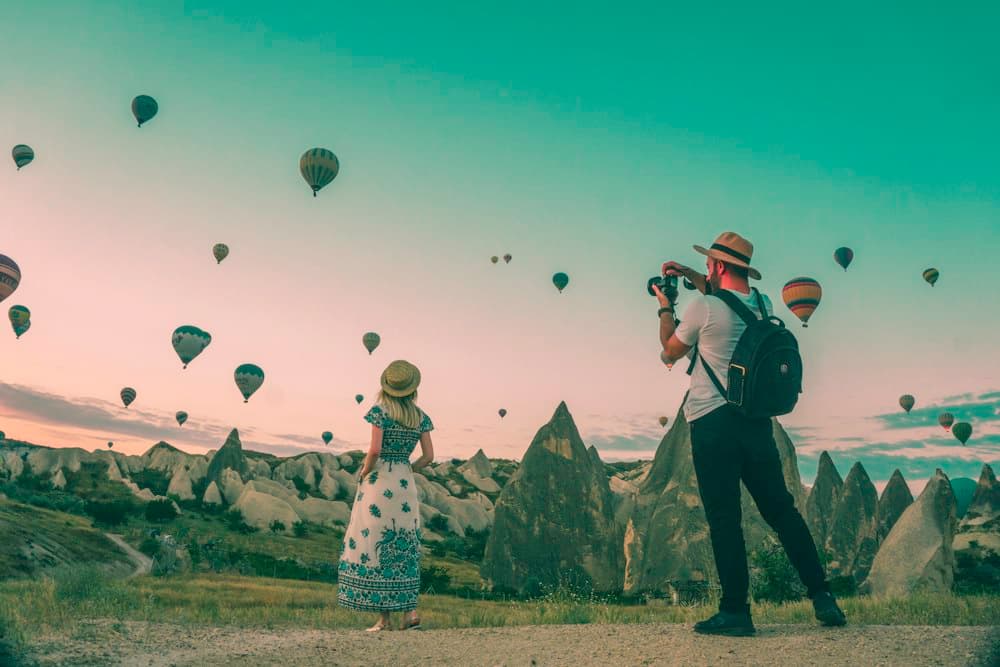 Travellers watching hot air balloons rise over rock formations at sunrise